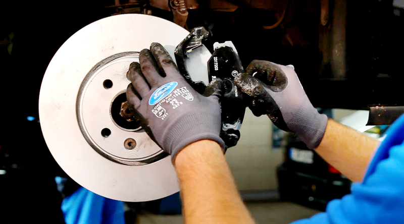 Auto-Ersatzteile Mechanikerhände an einer Bremsscheibe